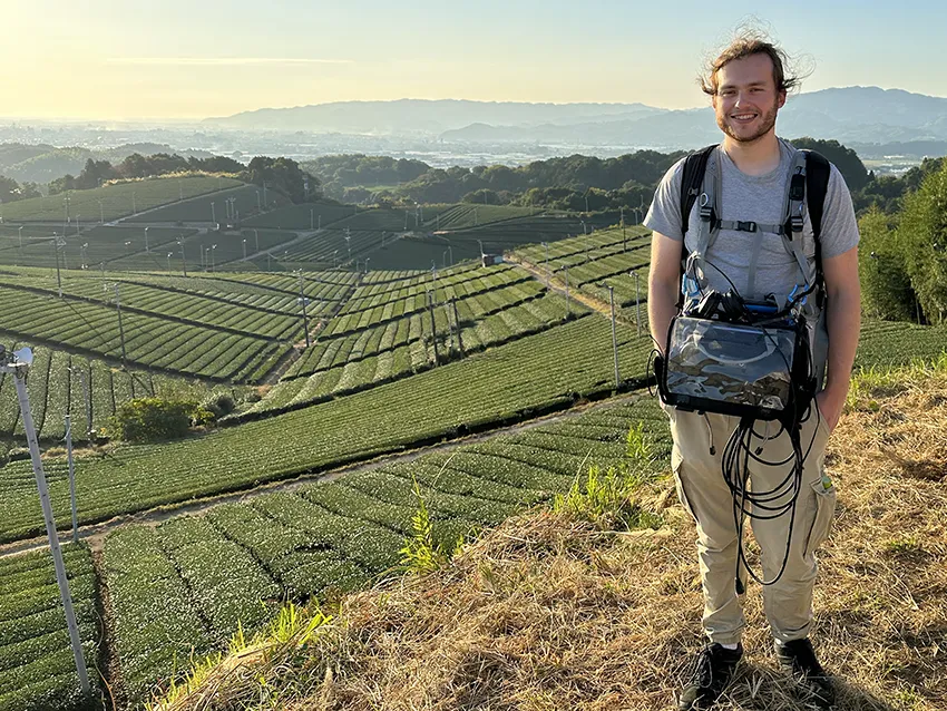 Gavin Winterborn holding sound equipment on location with mountains in the background.